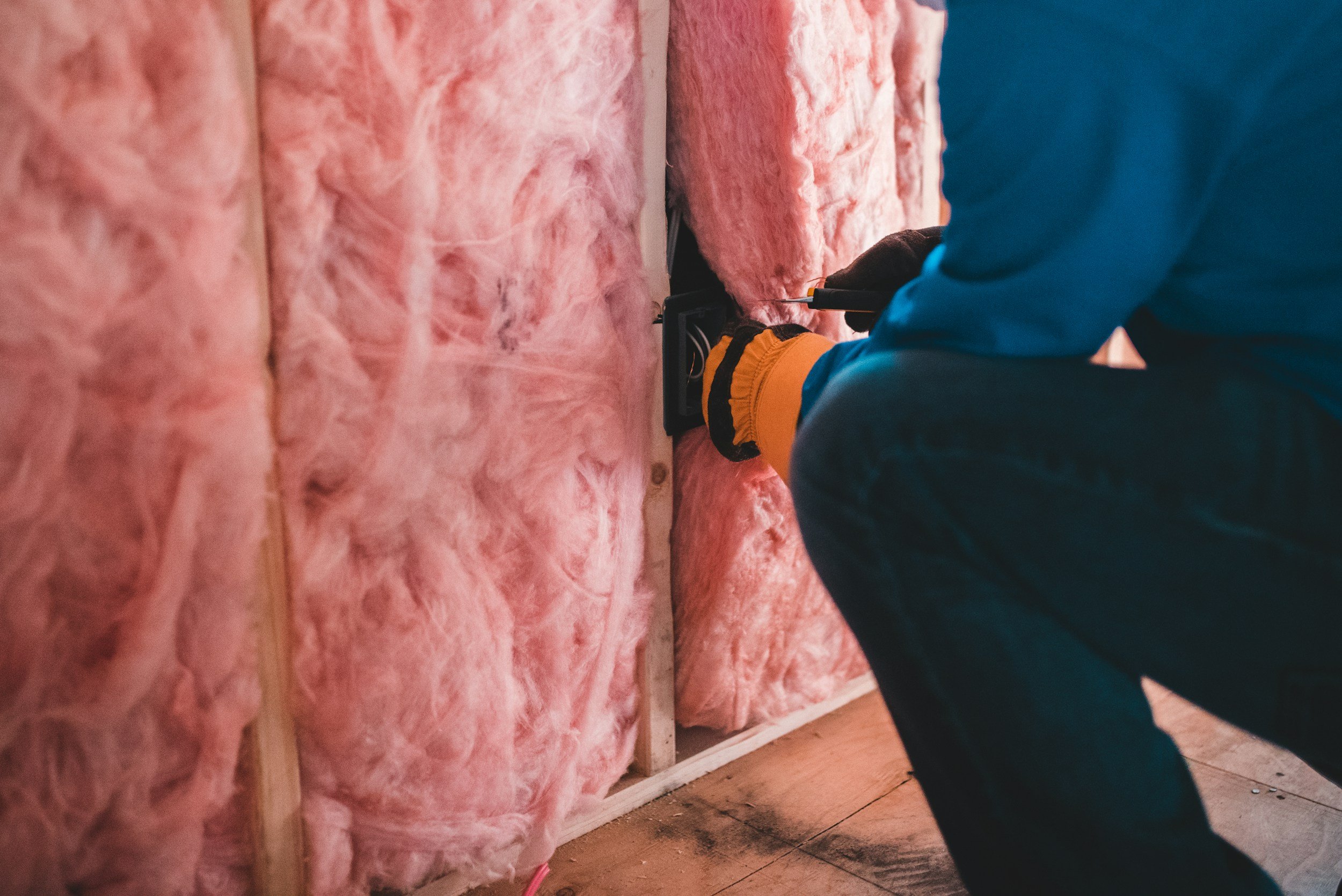 Worker installing pink insulation in a wall frame