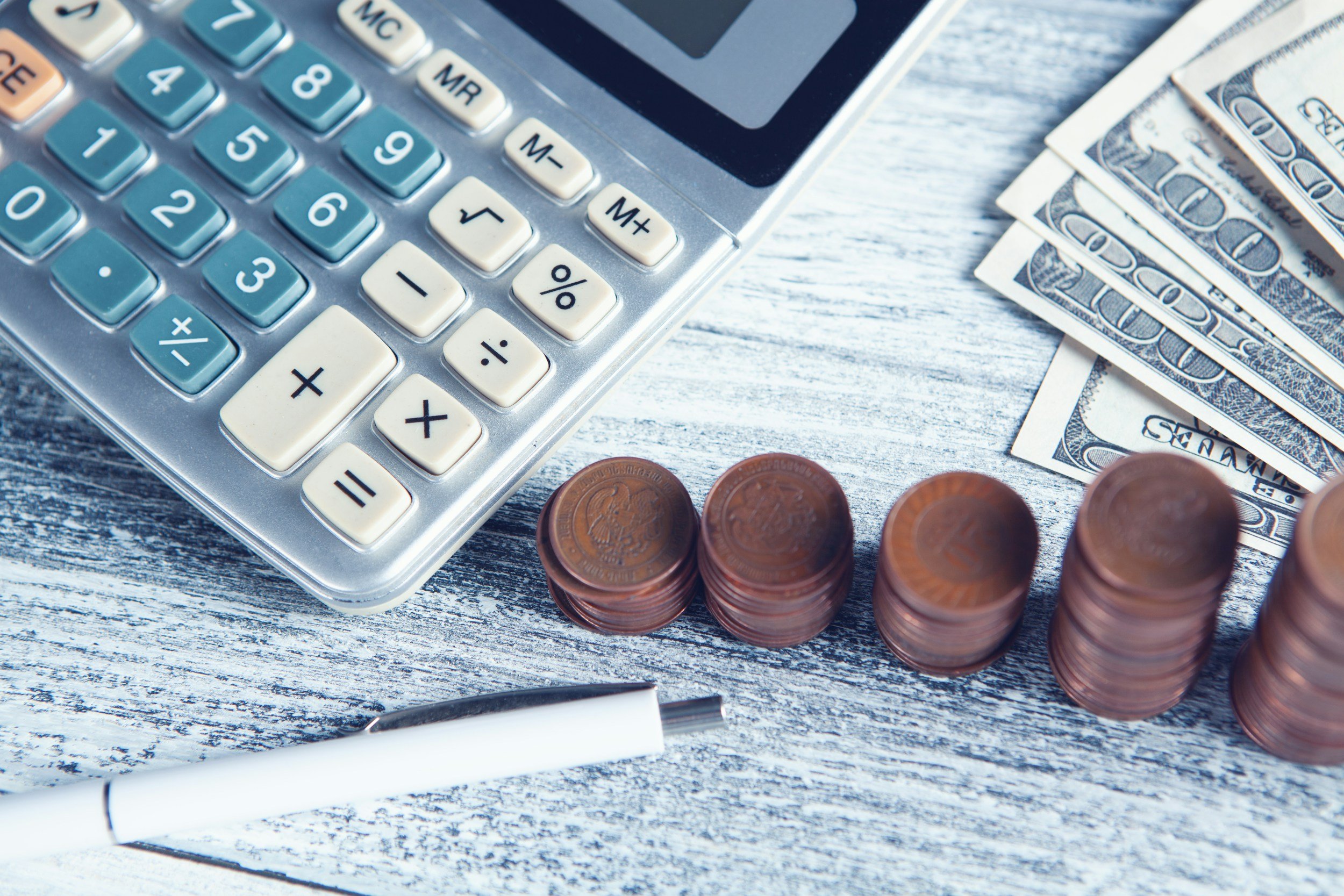 Calculator, dollar bills, and stacked coins on a wooden desk